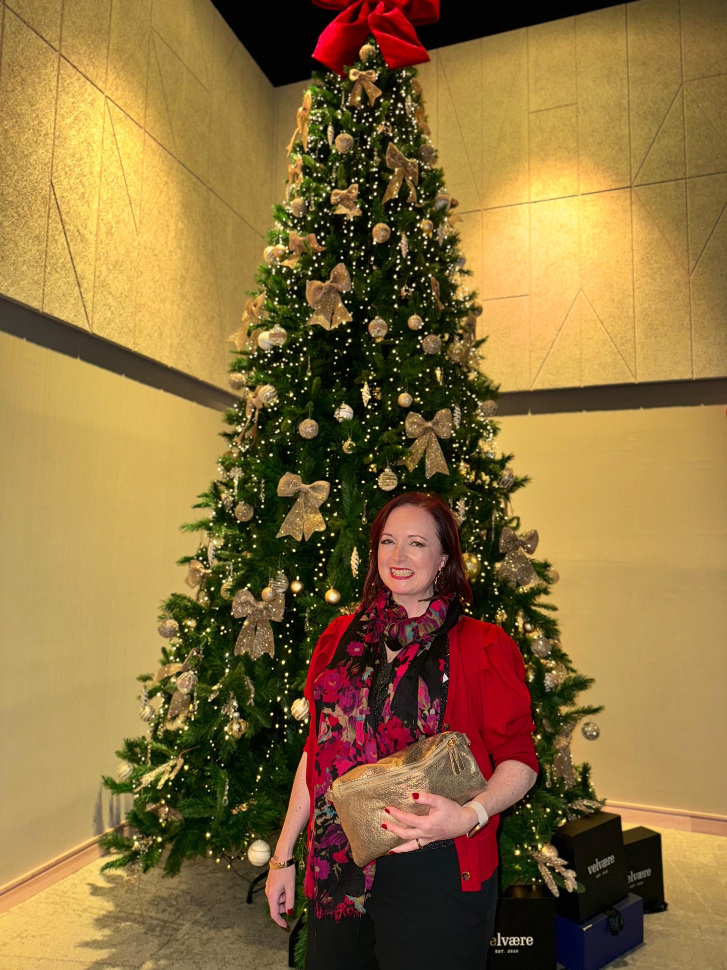 Dark haired lady standing in front of a Christmas tree wth a Pchette Póca Handbag in Gold