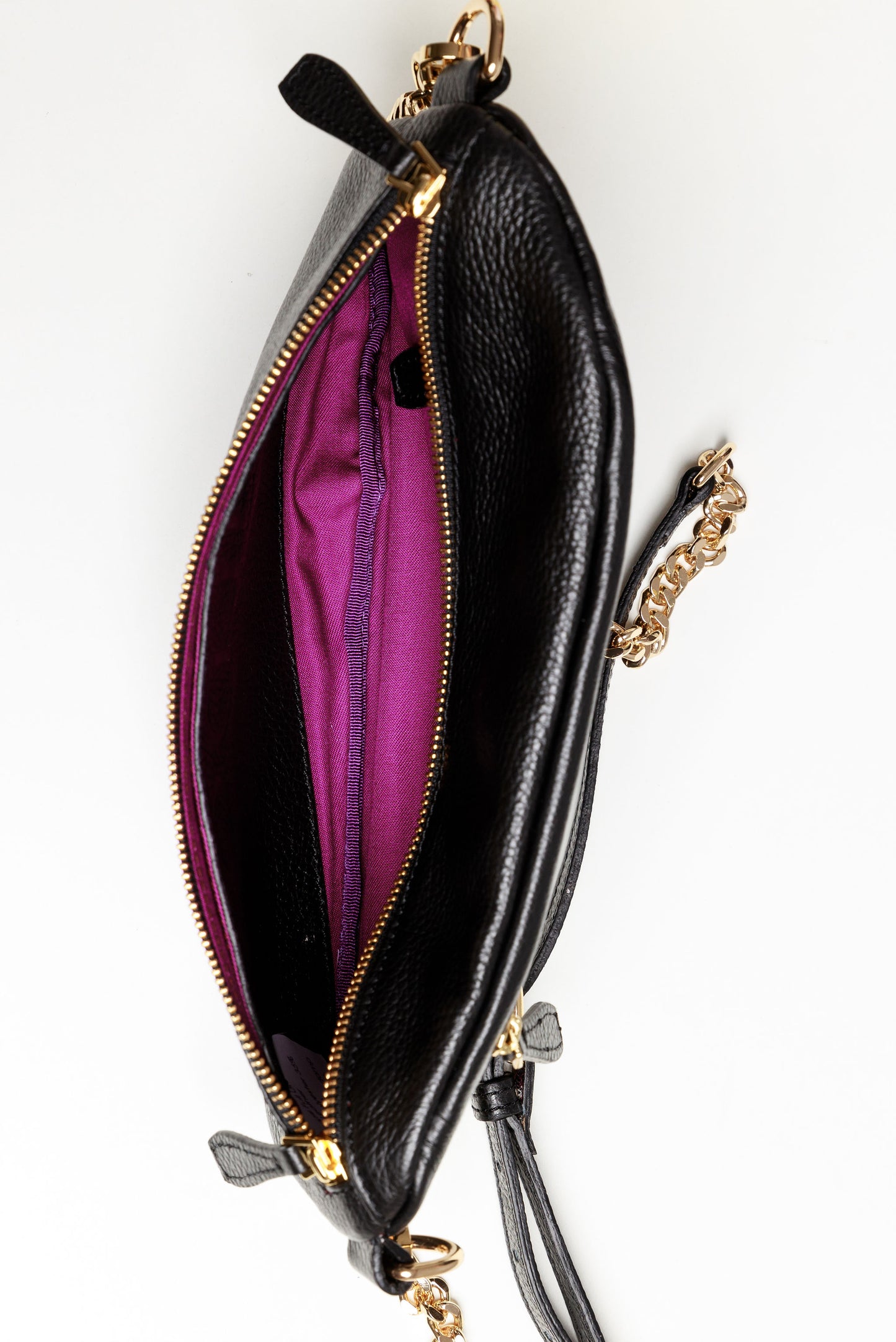 The inside of a black Póca swing bag showing the brightly coloured syrah lining and a front leather flap pocket.