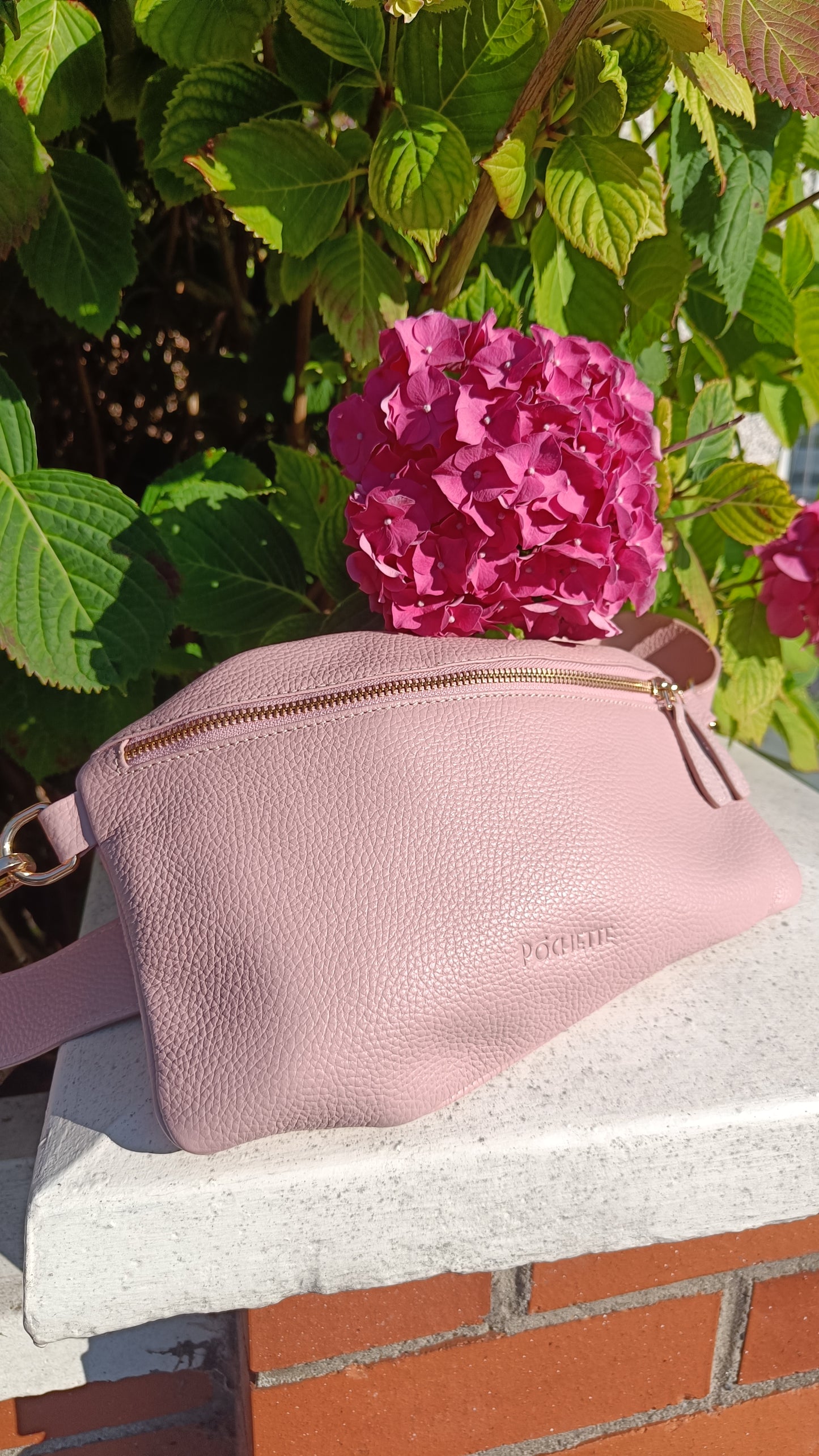 Powder Pink Póca handbag on a wall in front of a beautiful bright pink hydrangea