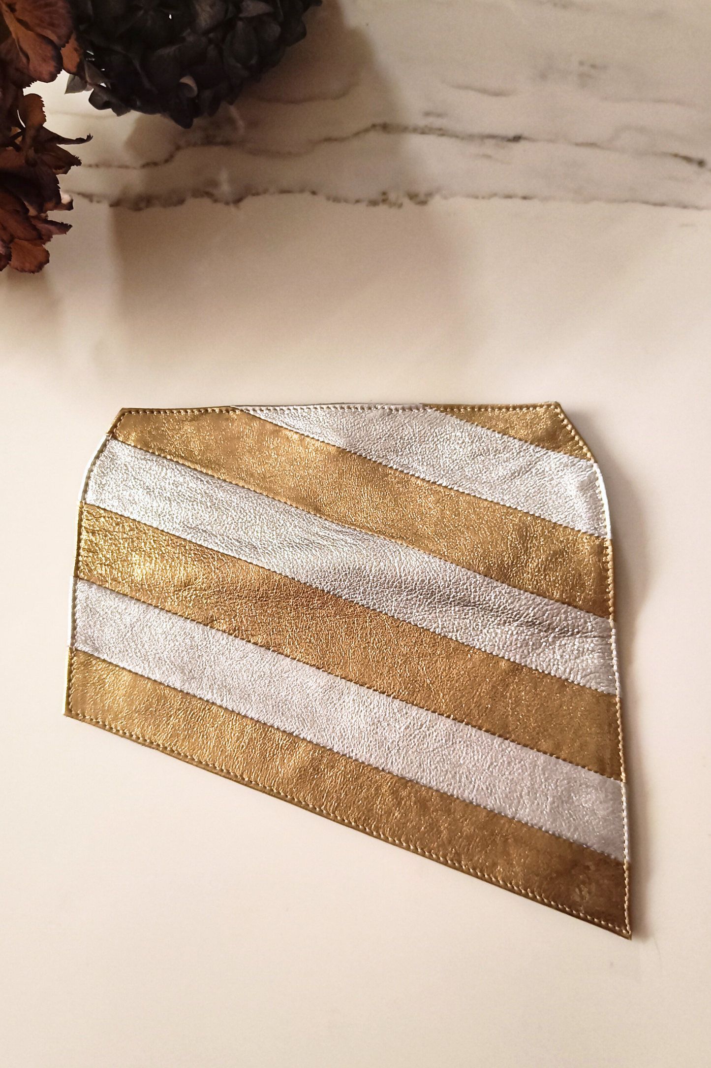 Gold and silver striped leather cover for a Póchette Danu handbag on a marble surface