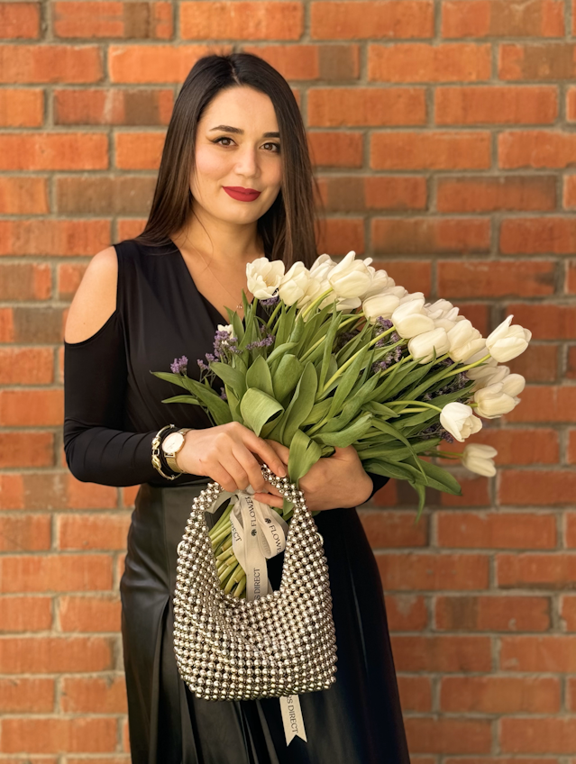 A photos of a dark harded woman wearing a black top and black leather skirt holding a bunch of white tulips and a beautiful silver beaded handbag