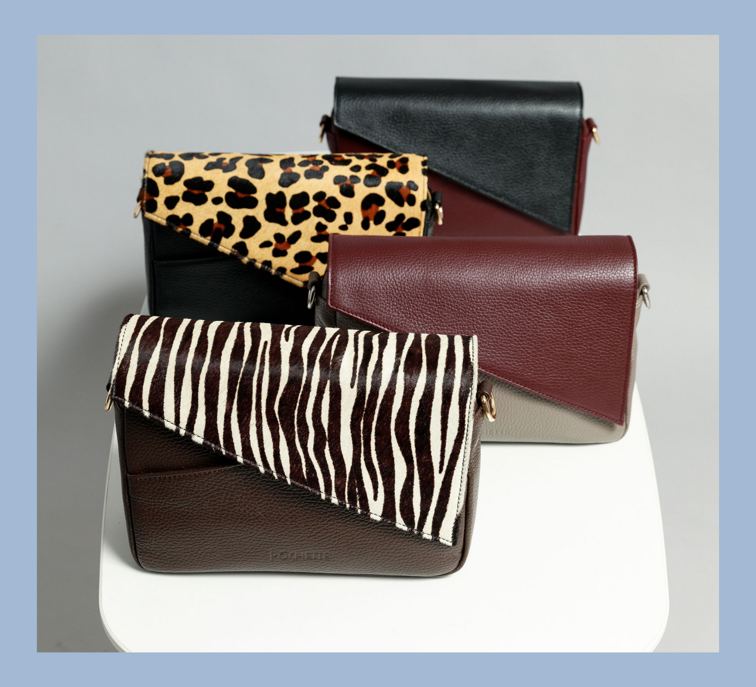 Four crossbody bags on a white surface with a grey background. From the back you can see a black leather flap on a burgundy crossbody bag, the next closest bag is black with a leopard print flap. This is followed by a pottery clay bag with a burgundy flap. At the front is a chocolate brown crossbody bag with a zebra print flap.