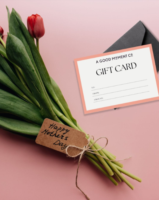 A gift card for A Good Moment Company palced beside a bunch of red tulips on a ping background