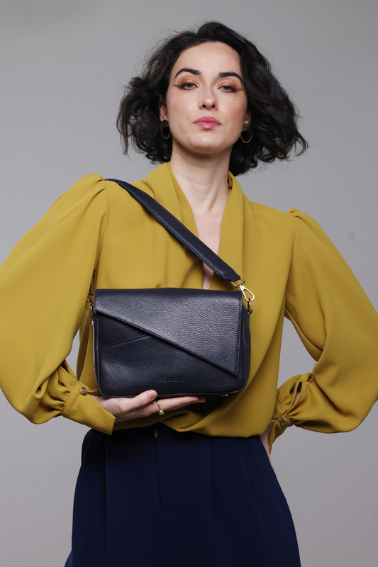 A dark haired woman wearing a mustard yellow blouse, navy pants and a navy blue leather handbag