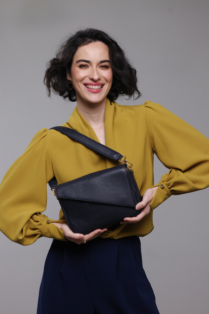 A dark haired woman wearing a mustard yellow blouse, navy pants and a navy blue leather handbag