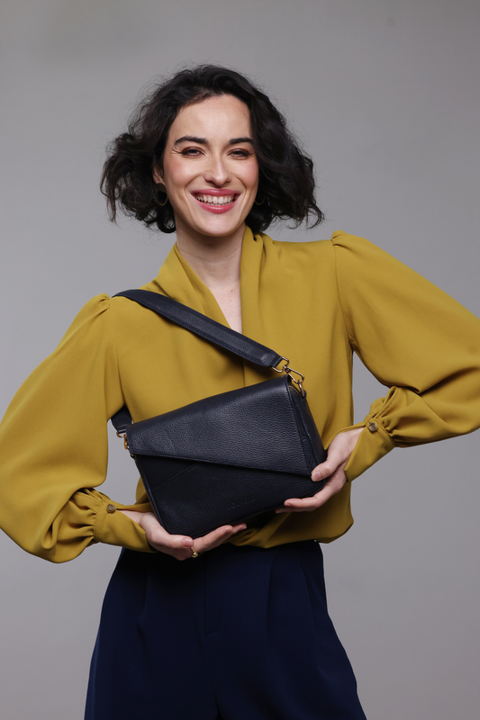 A dark haired woman wearing a mustard yellow blouse, navy pants and a navy blue leather handbag