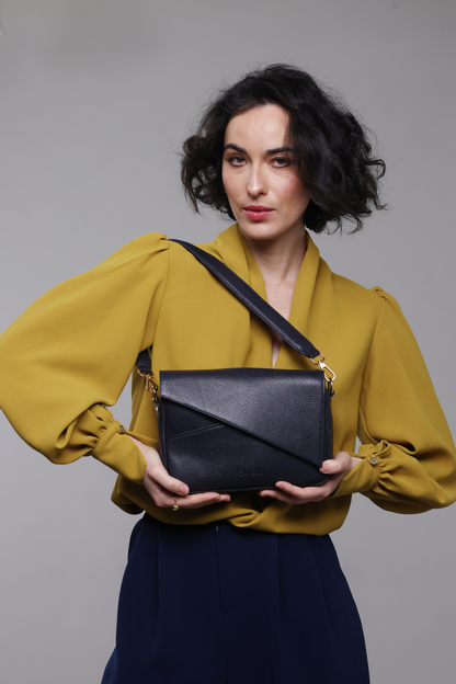 A dark haired woman wearing a mustard yellow blouse, navy pants and a navy blue leather handbag