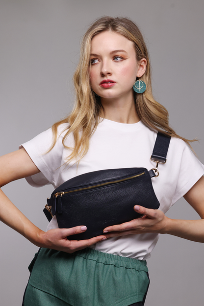 A blonde haired woman wearing a white t-shirt, a teal and denim skirt and a navy blue leather crossbody bag.