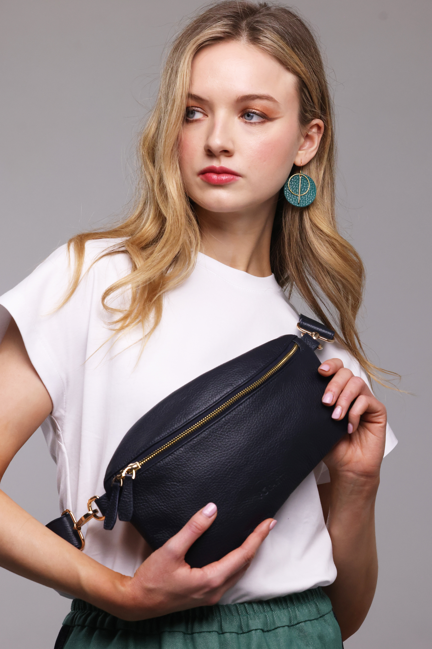A blonde haired woman wearing a white t-shirt, a teal and denim skirt and a navy blue leather crossbody bag.