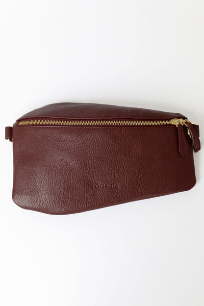 A burgundy swing crossbody bag, called the Póca, on a white surface.