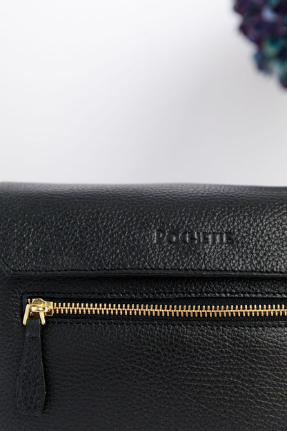 A close up of the black crossbody bag with blurred hydrangeas in the background. The zipped pocket at the back and the Póchette brand are displayed.