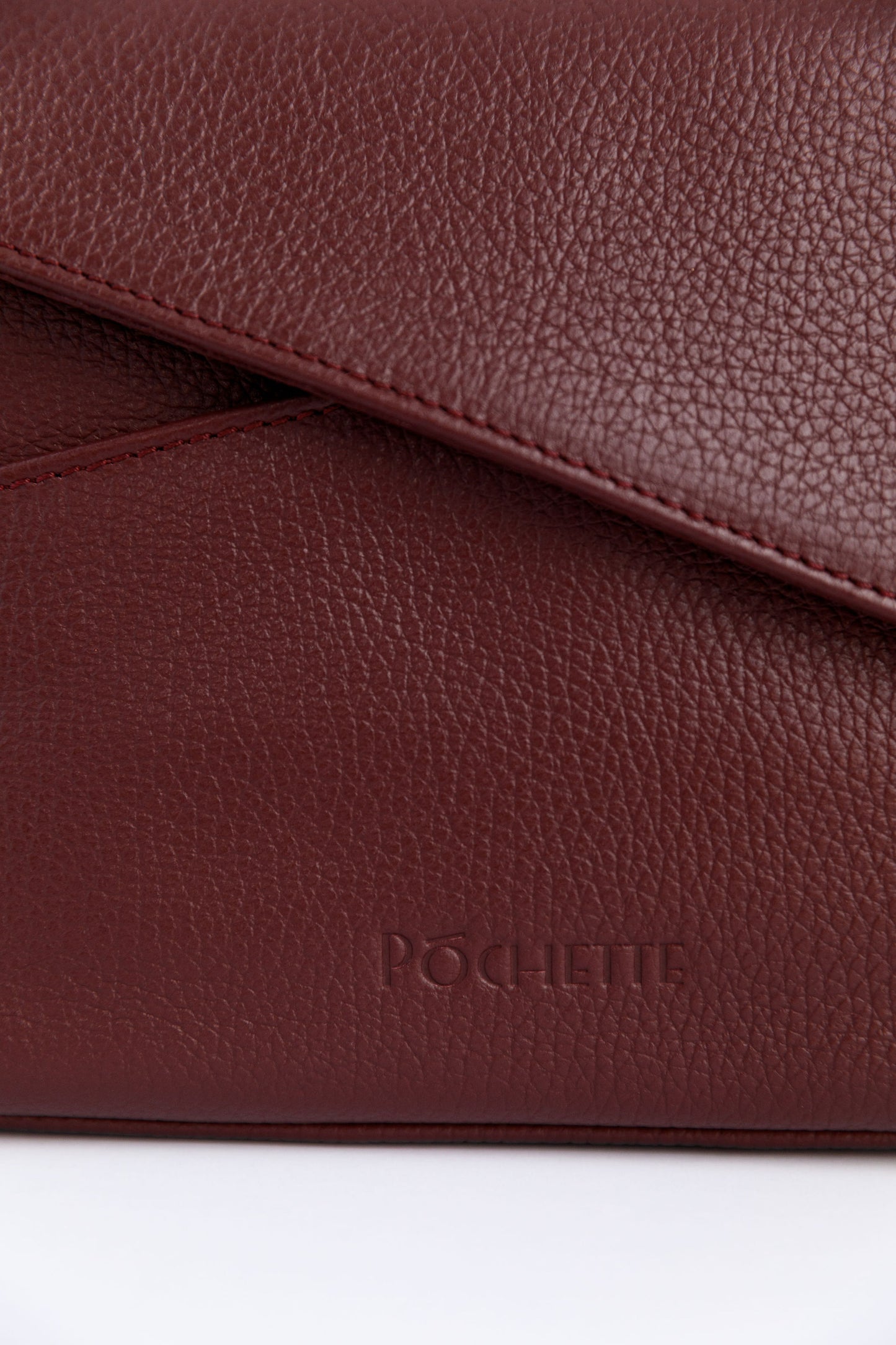 A close up of the Póchette logo on the burgundy crossbody bag.