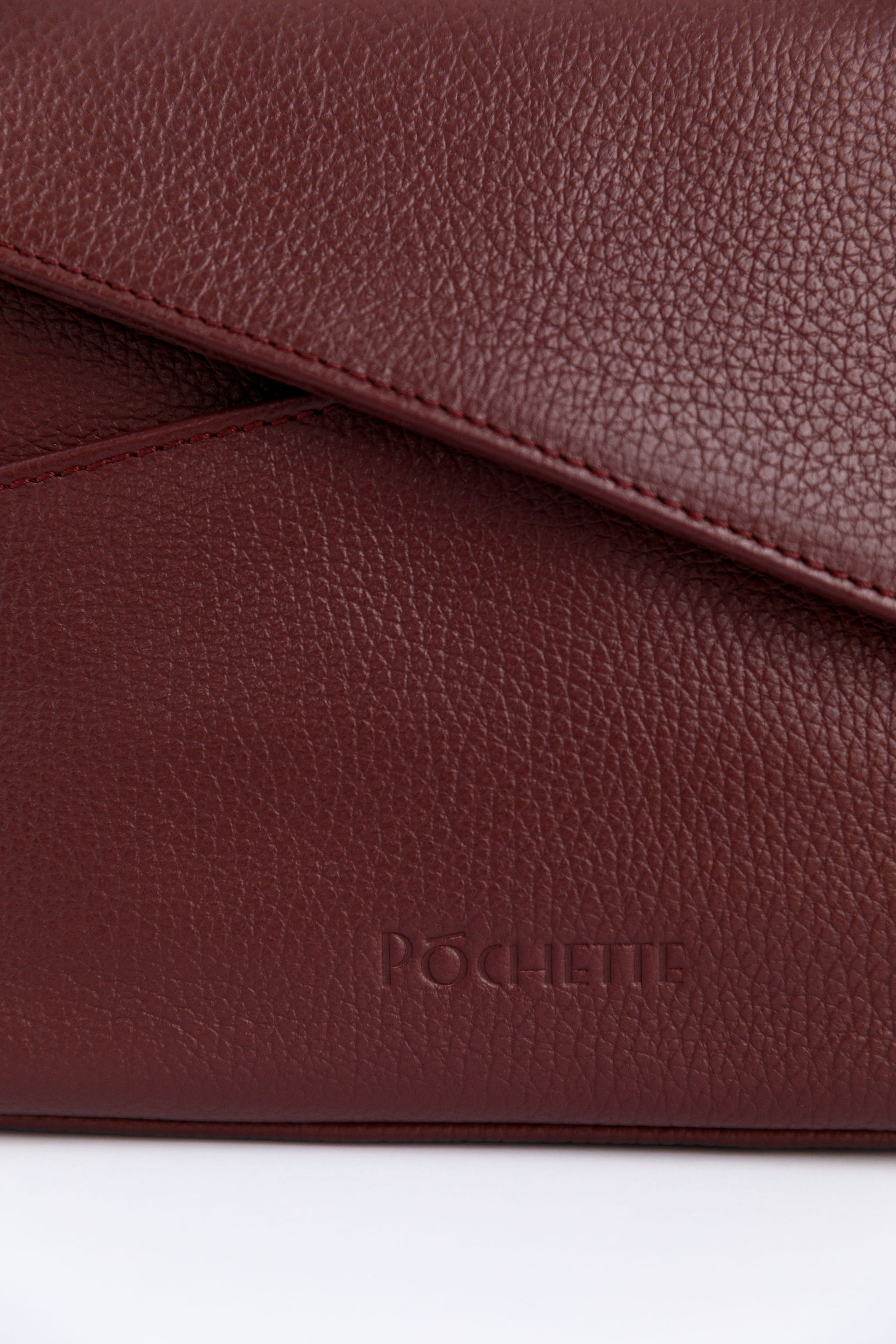 A close up of the Póchette logo on the burgundy crossbody bag.