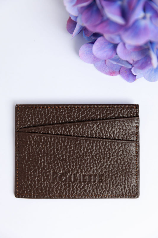 A chocolate card wallet on a white surface with a blurred hydrangea in the foreground.