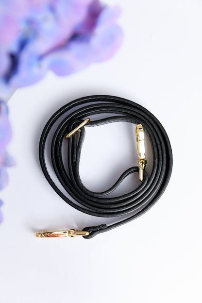 A black thin leather strap on a white surface with a blurred hydrangea in the foreground.