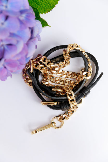 A black leather and chain strap on a white surface with a blurred hydrangea in the foreground.