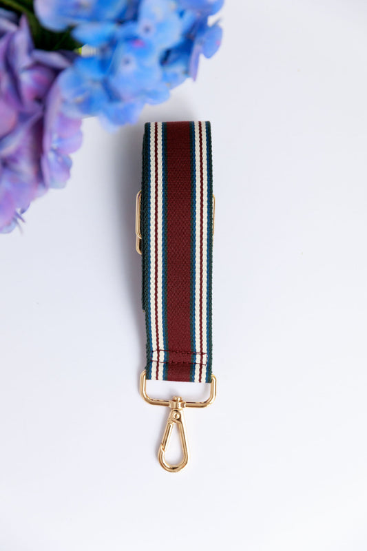 A burgundy striped woven strap on a white surface with a blurred hydrangea in the foreground.