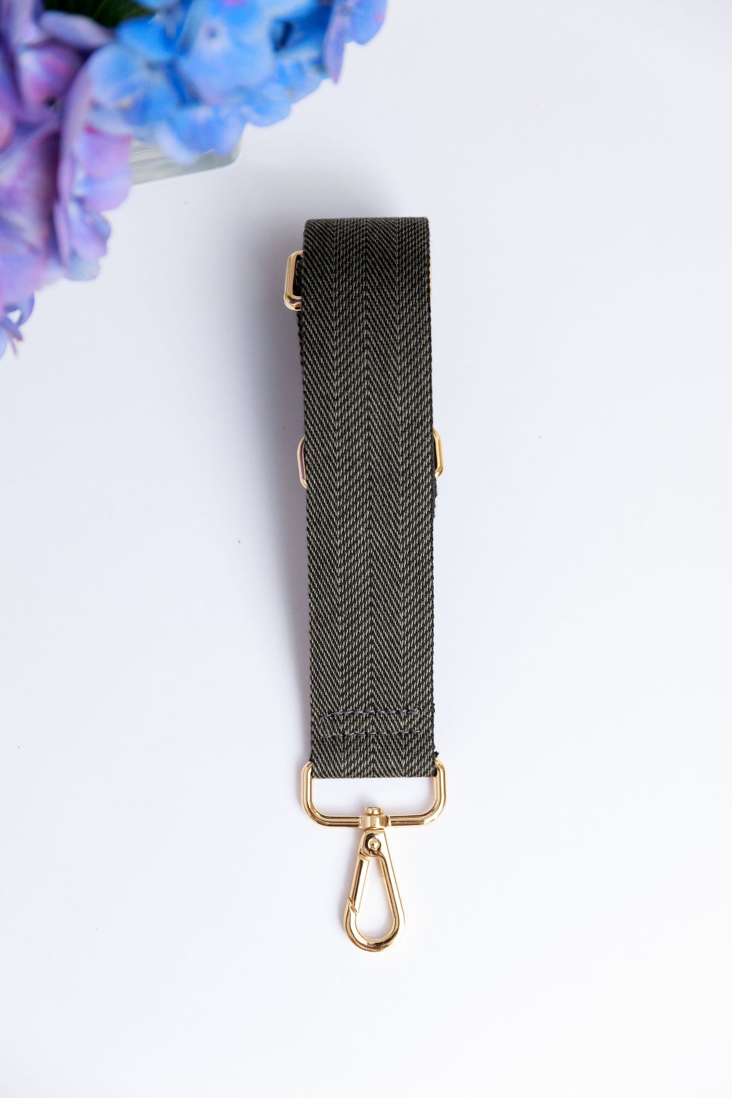 A black woven strap on a white surface with a blurred hydrangea in the foreground.