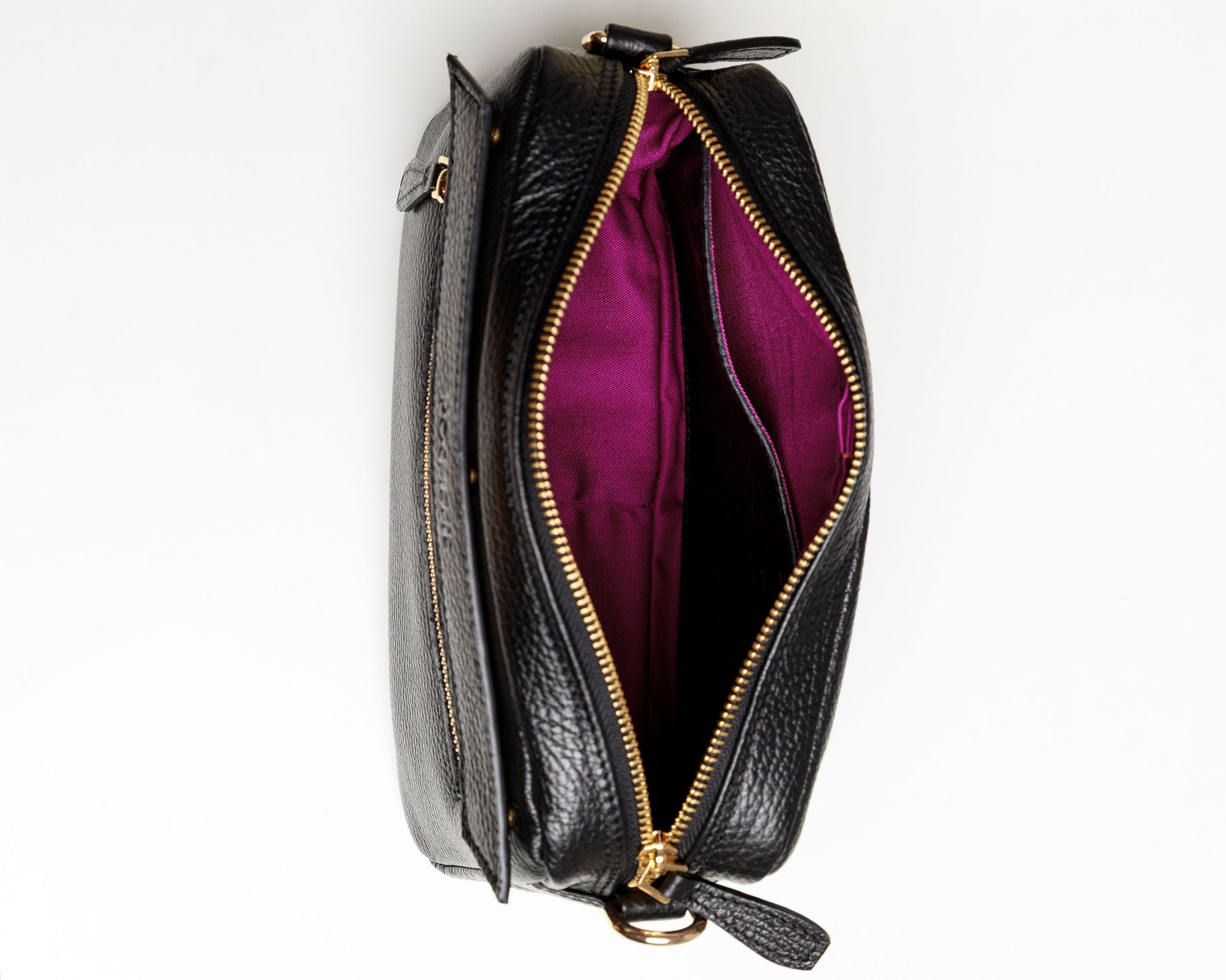 The inside of a black crossbody bag showing the brightly coloured syrah lining and a front leather flap pocket. 