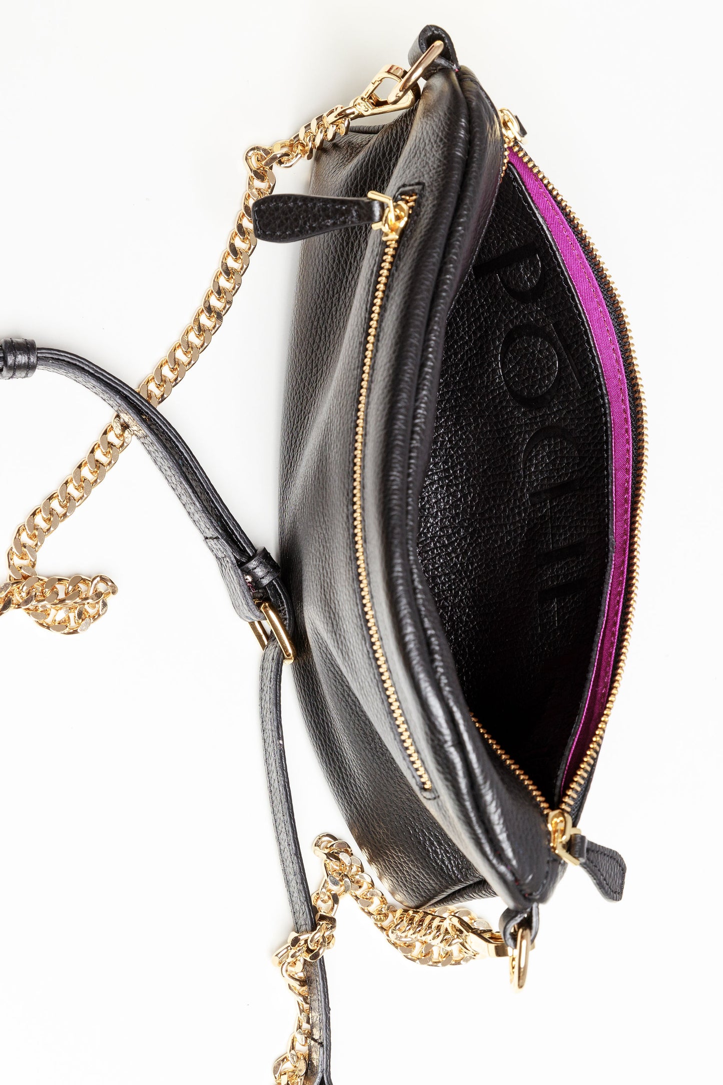 The inside of a black Póca swing bag showing the brightly coloured syrah lining and a front leather flap pocket. 