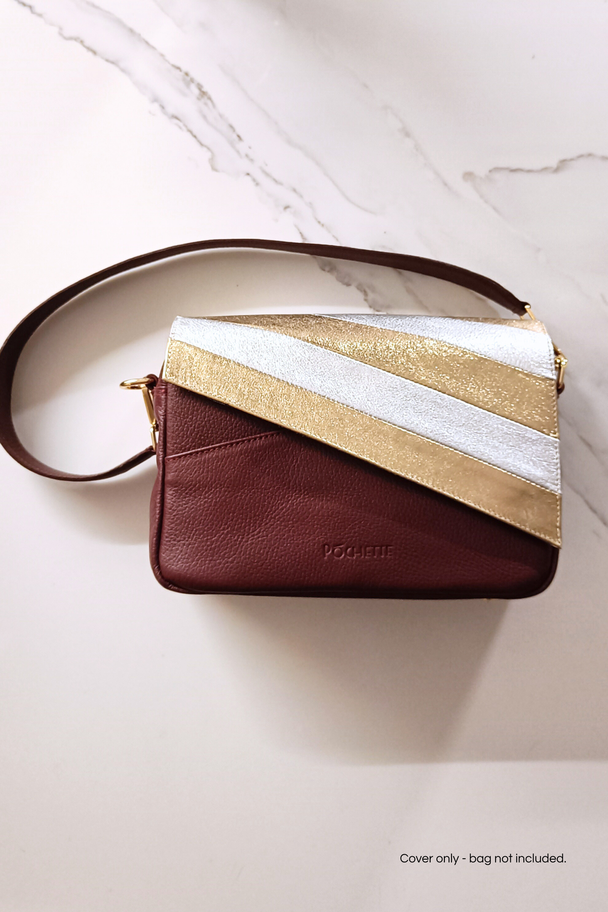 A burgundy leather crossbody bag with a diagonal flap featuring metallic gold and silver stripes, displayed on a white marble surface.