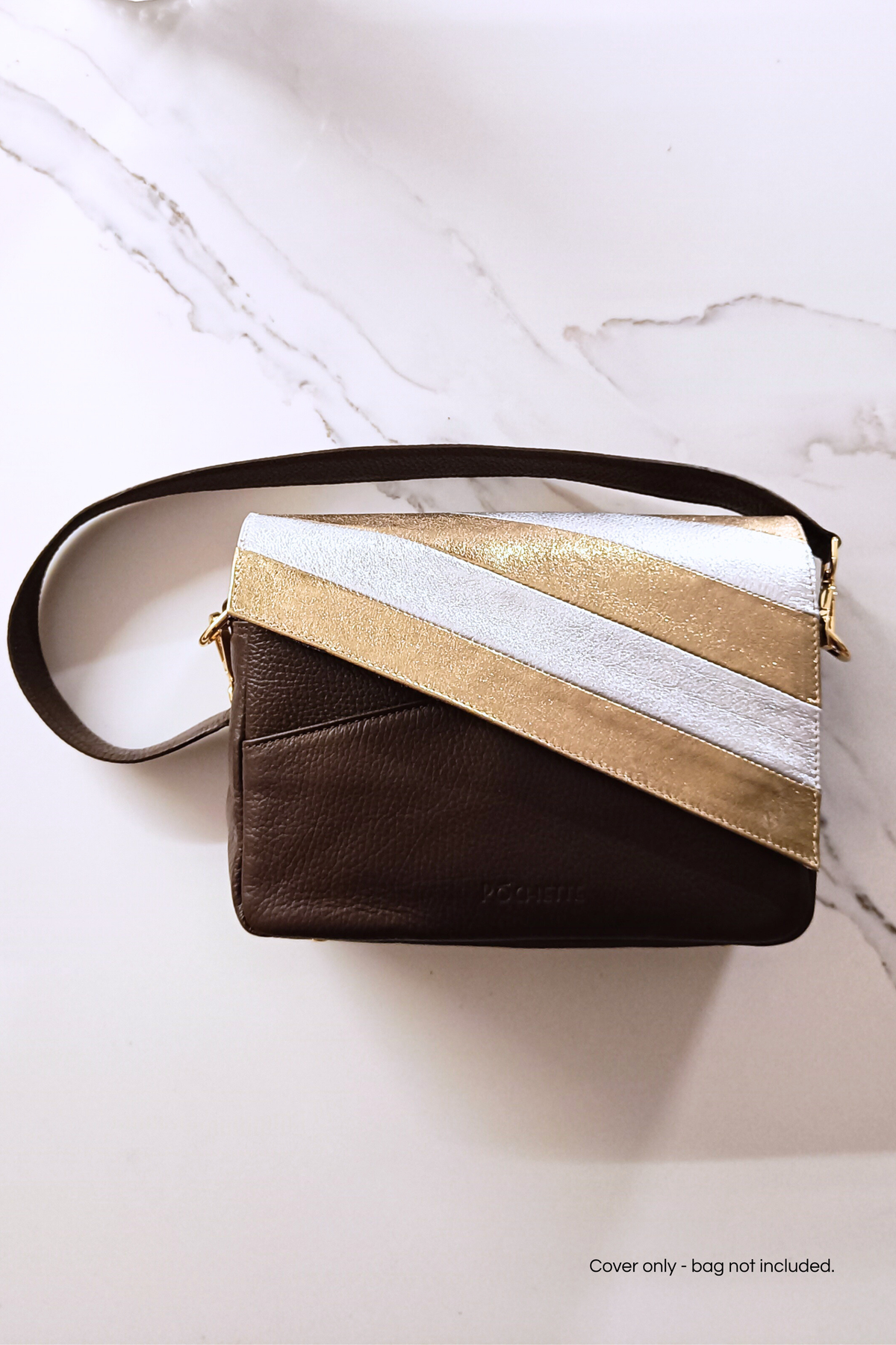A dark brown leather crossbody bag with a diagonal flap featuring metallic gold and silver stripes, displayed on a white marble surface.