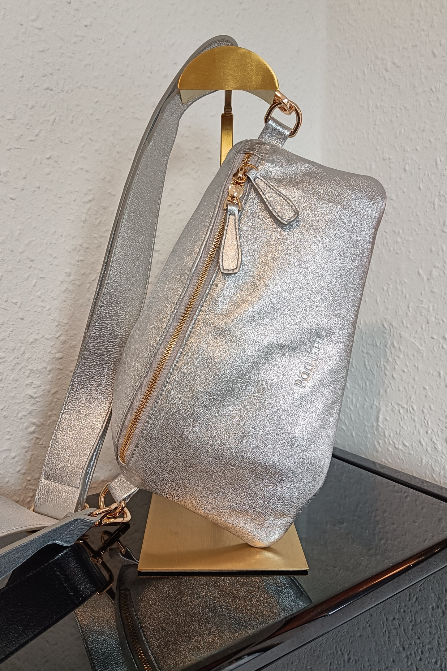 Sparkle Póca handbag in Silver with a statement leather strap on a gold stand