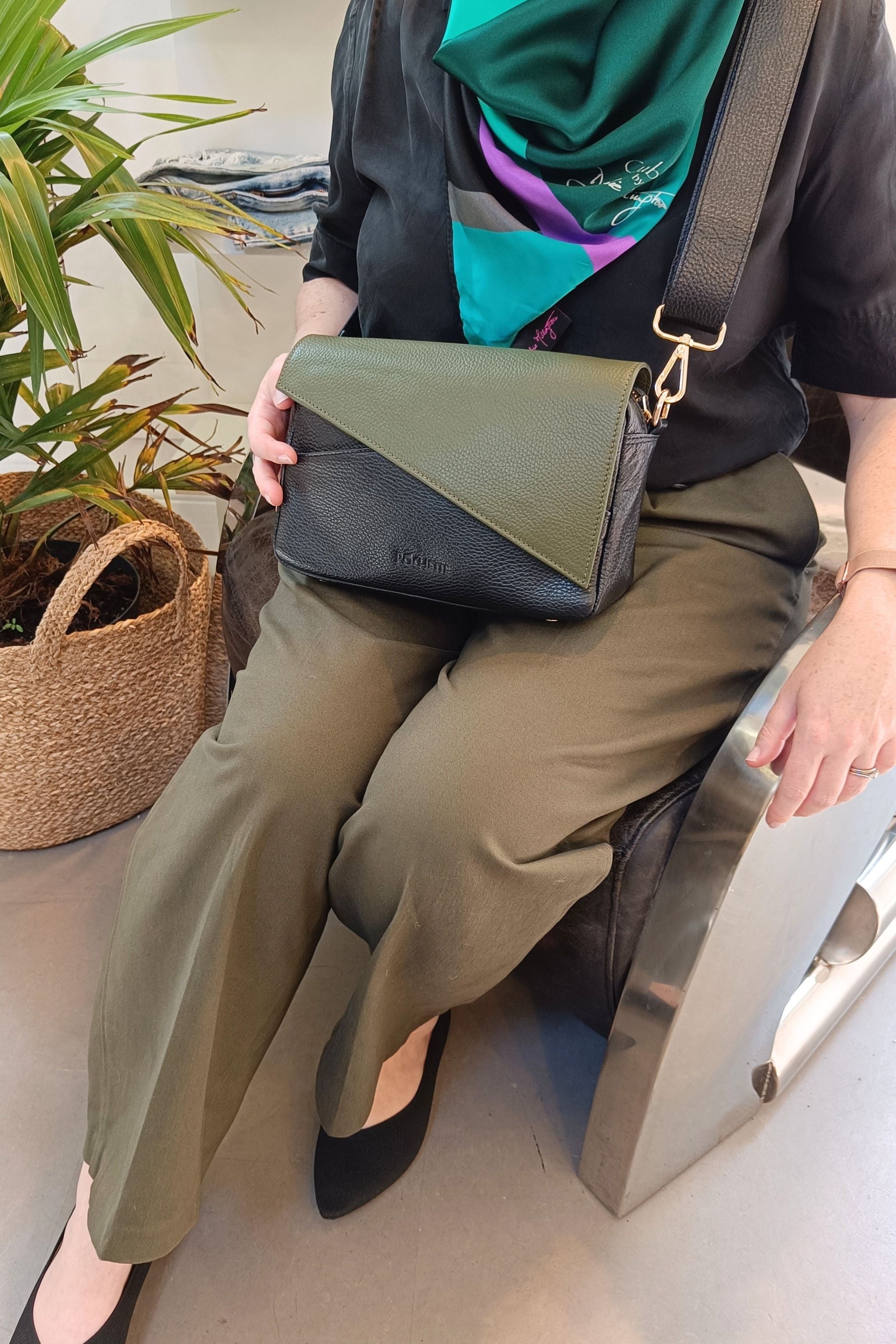 Person sitting on a chair holding a black and green handbag with a plant in the background