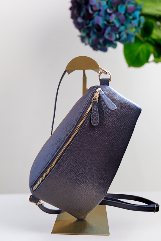 Navy blue handbag on a gold stand with a blurred flower in the background