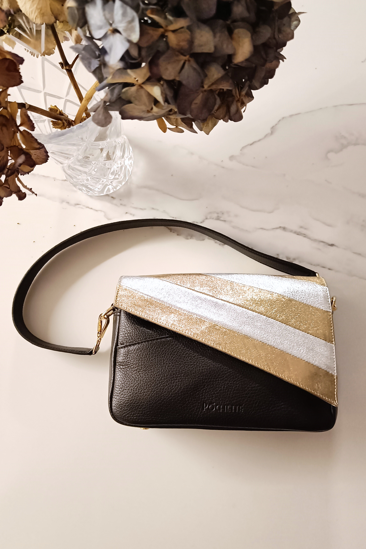 Gold and silver striped leather cover on a black Póchette Danu handbag on a marble surface