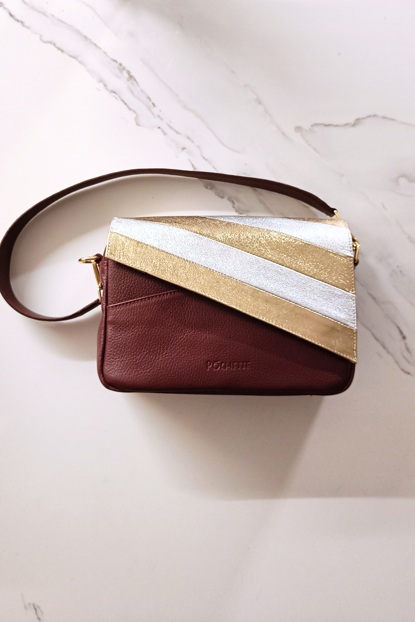 Gold and silver striped leather cover on a burgundy Póchette Danu handbag on a marble surface