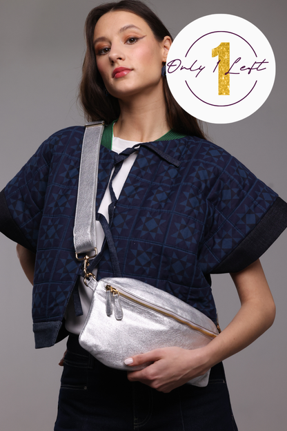 A woman wearing a navy blue patterned kimono jacket and dark jeans, wearing a shiny silver crossbody bag with a wide silver strap. A white circular badge in the top right corner reads 'Only 1 Left' with a gold '1'.