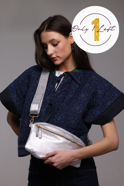 A woman wearing a navy blue patterned kimono jacket and dark jeans, wearing a shiny silver crossbody bag with a wide silver strap. A white circular badge in the top right corner reads 'Only 1 Left' with a gold '1'.