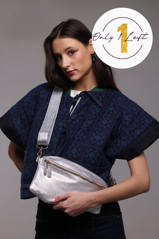A woman wearing a navy blue patterned kimono jacket and dark jeans, wearing a shiny silver crossbody bag with a wide silver strap. A white circular badge in the top right corner reads 'Only 1 Left' with a gold '1'.