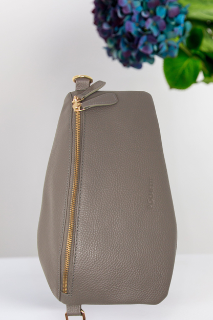 Gray leather bag with gold zipper on a white background with flowers in the background