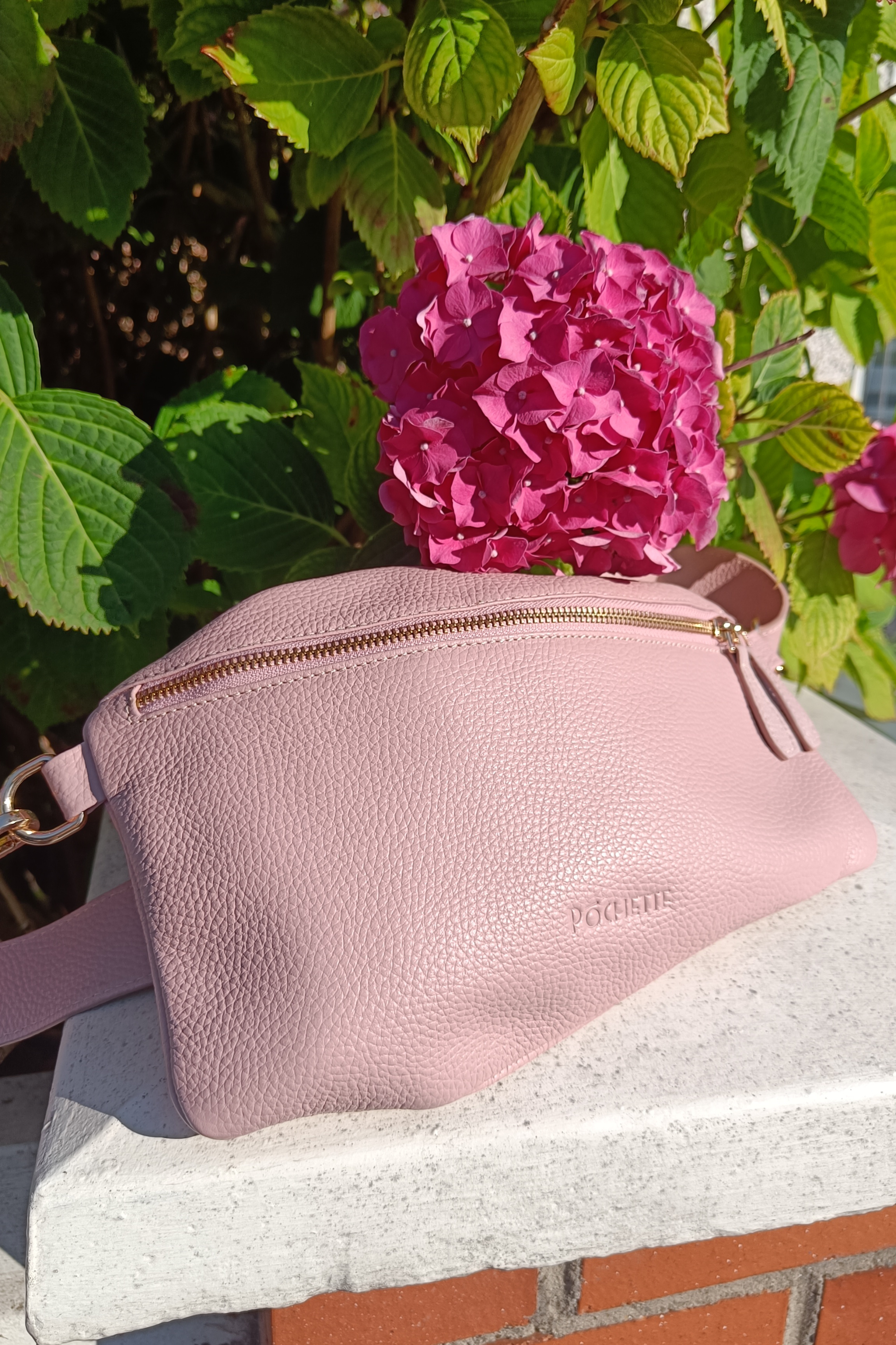 Powder Pink Póca handbag on a sunny day with a bright pink hydrangea beside it