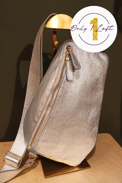 A metallic silver handag with gold-tone zippers, displayed on a gold stand against a dark green background. A white circular badge in the top right corner features a gold '1' and the text 'Only 1 Left'.
