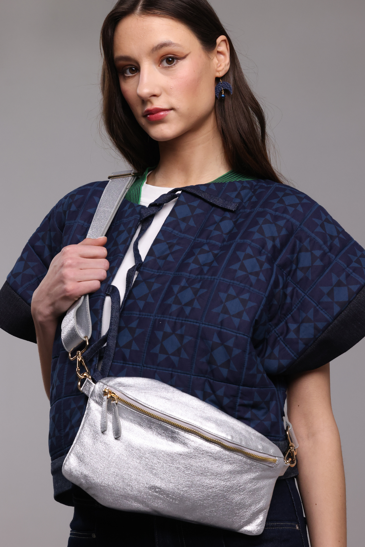 Woman holding a silver crossbody bag against a gray background